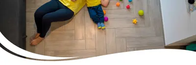 An adult parent and a child laying on their back on the floor both wearing a yellow shirt and jeans surrounded by toys.