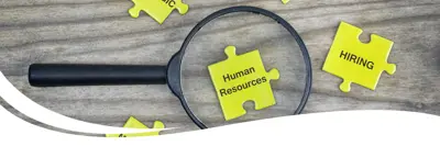A magnifying glass with puzzle pieces around it that say hiring and people.